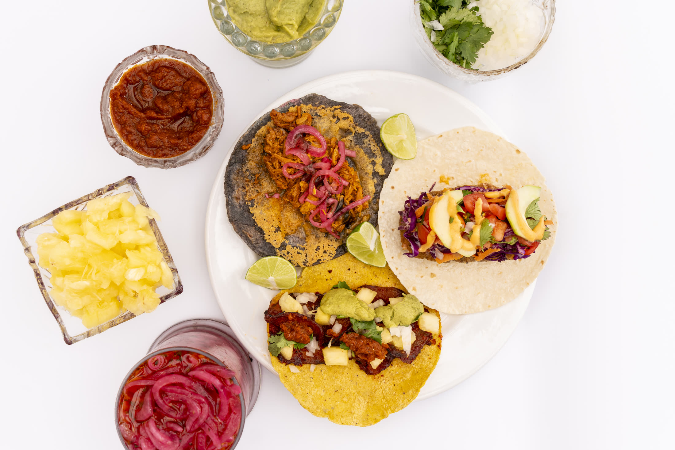 Three tacos on a white plate with lime wedges